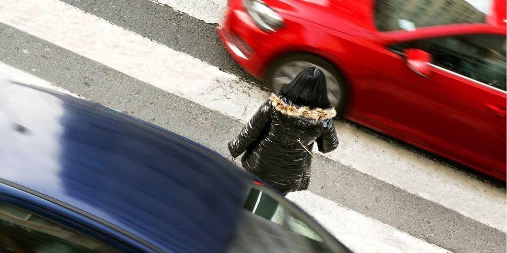 Woman walking across street near red car, relevant