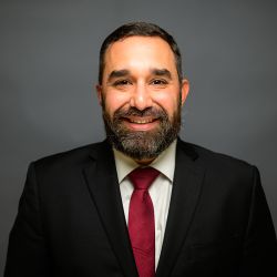Benjamin J. Vazquez in a suit with a red tie against a gray background.