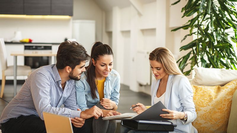 Young professionals reviewing documents in a modern living room setting with a laptop and green plant nearby.