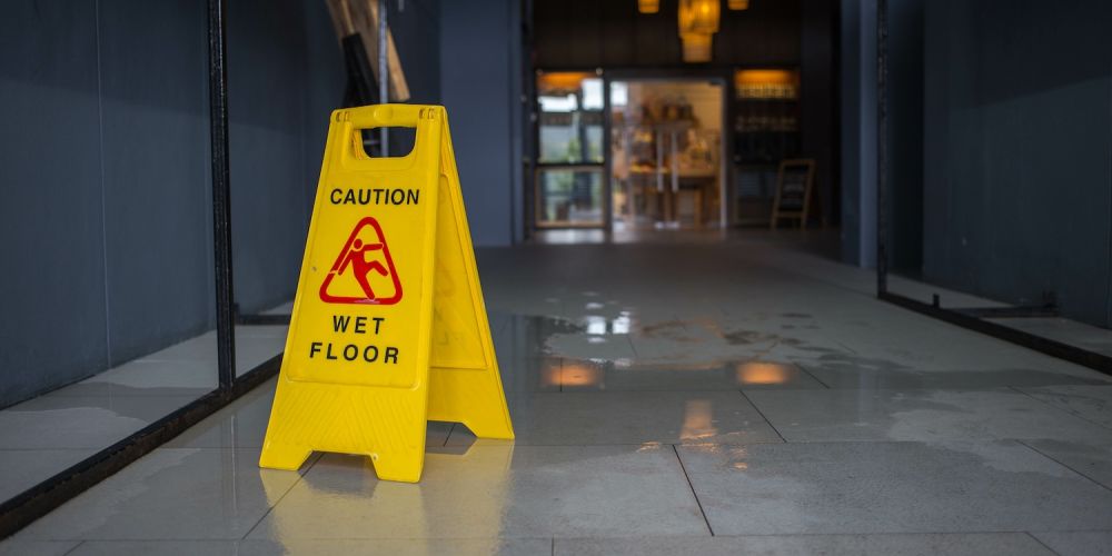 Yellow caution sign on wet floor in hallway, highlighting safety warning in dimly lit interior space.