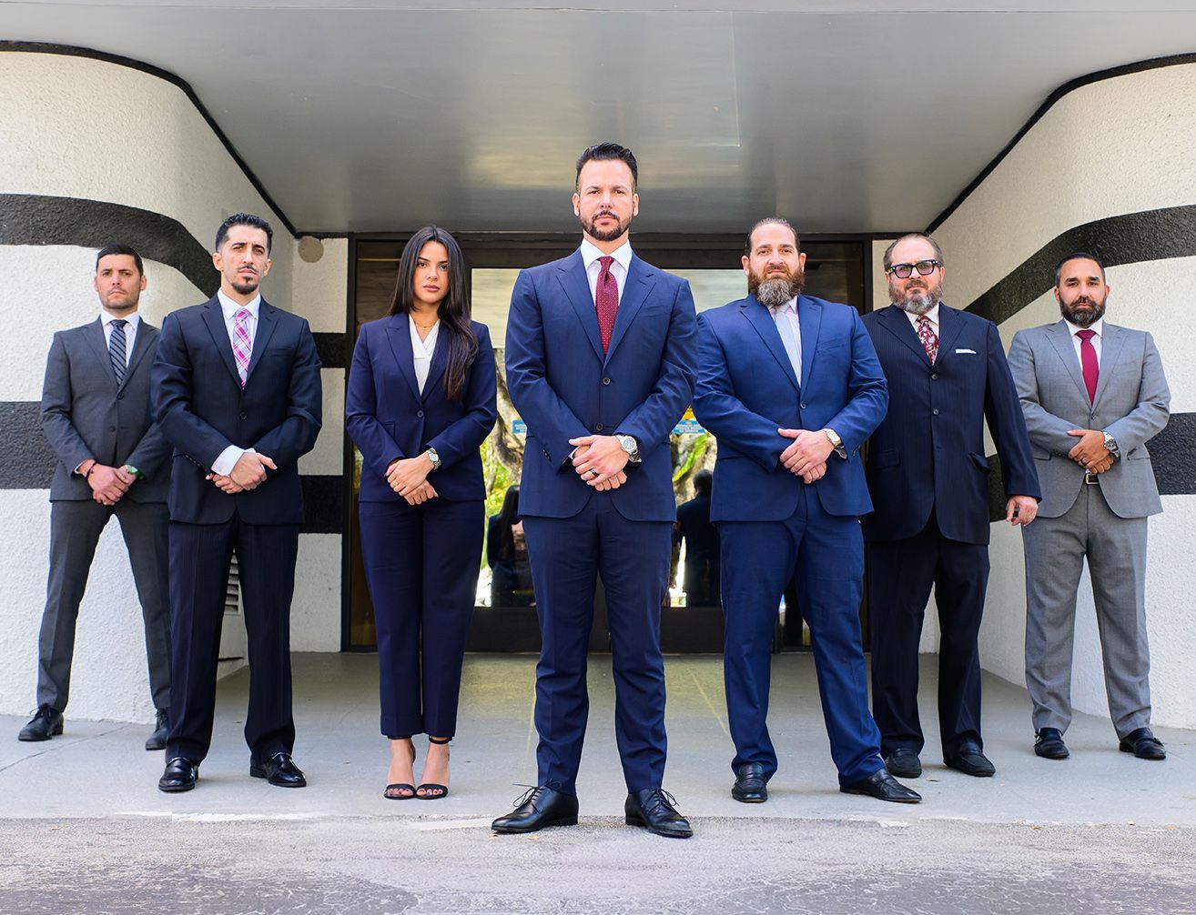 Professional team in suits posed confidently outside modern office building.