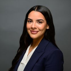 Professional woman in a navy blazer smiling confidently against a gray background.