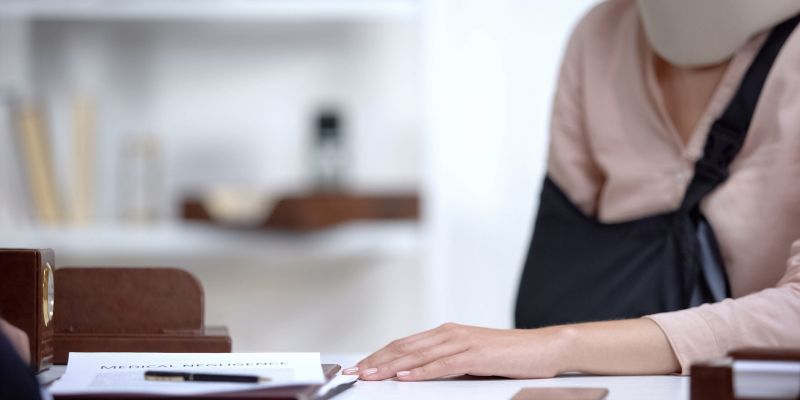 Injured woman with neck brace and arm sling at desk with medical negligence documents.