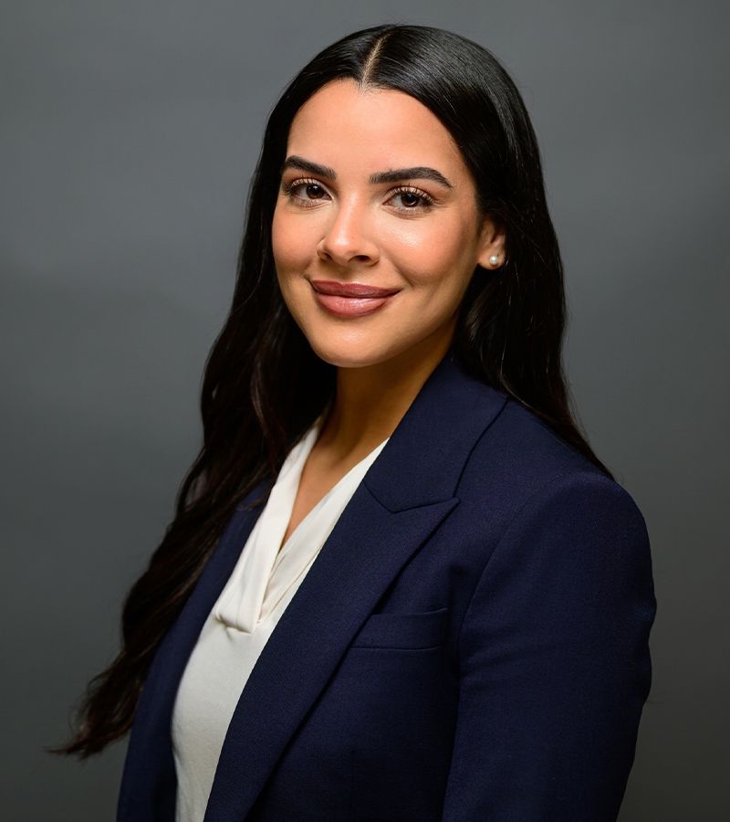 Professional woman in a navy blazer smiling confidently against a gray background.