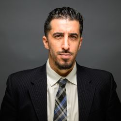 Jorge A. Abreu in a suit with striped tie, dark background, looking confident.