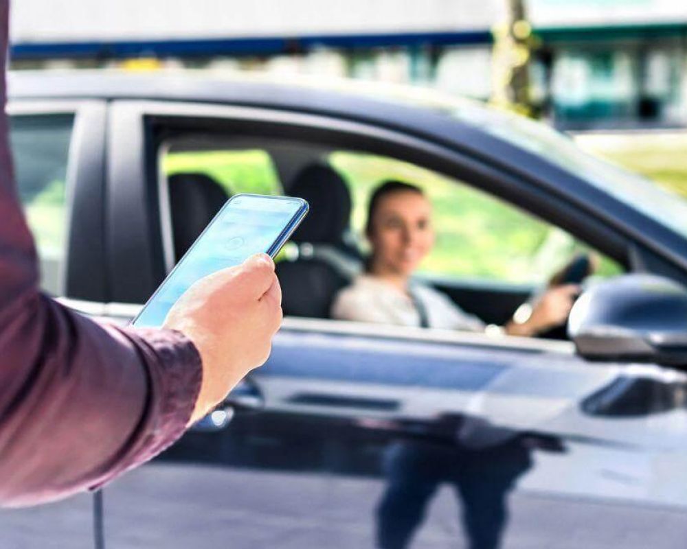 Persona con celular frente a un coche, posiblemente