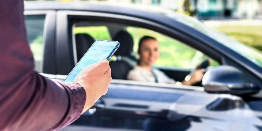 Persona con celular frente a un coche, posiblemente