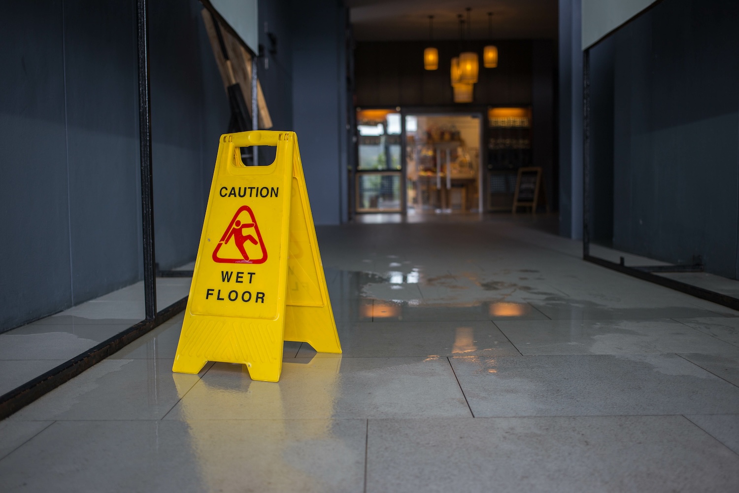 Yellow caution sign on wet floor in hallway, highlighting safety warning in dimly lit interior space.