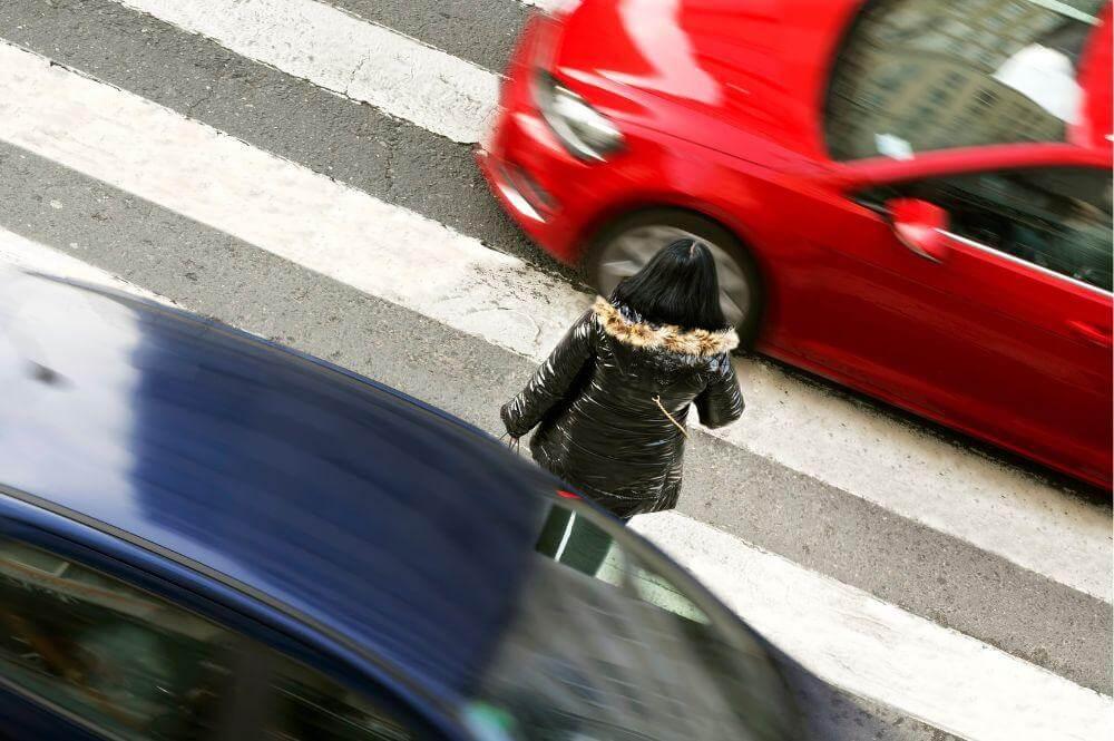 Woman walking across street near red car, relevant