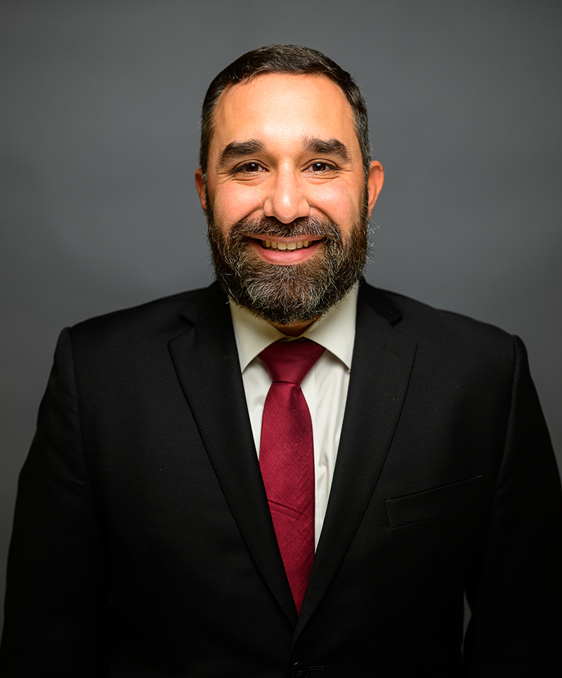 Benjamin J. Vazquez in a suit with a red tie against a gray background.
