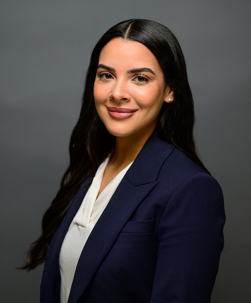 Professional woman in a navy blazer smiling confidently against a gray background.